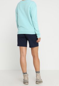 Světle modrá mikina s dlouhými rukávy, námořnické šortky a béžové kotníkové boty. Oblečení obsahuje vzorované ponožky.