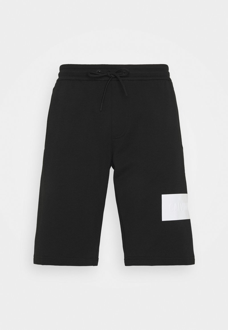 Shorts de survêtement noirs en tissu mélange de coton, dotés d'une taille élastique avec cordon de serrage et d'un patch logo blanc. Coupe standard.