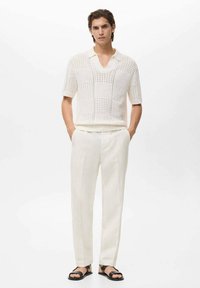 White knitted short-sleeve polo shirt with a textured pattern, paired with light-colored tailored pants and black sandals.