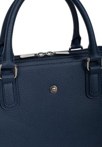 Granatowa torebka skórzana o fakturze pebble, z podwójnymi uchwytami na górze, z zamknięciem na zamek błyskawiczny i srebrnymi detalami. Posiada centralną płytkę z logo.