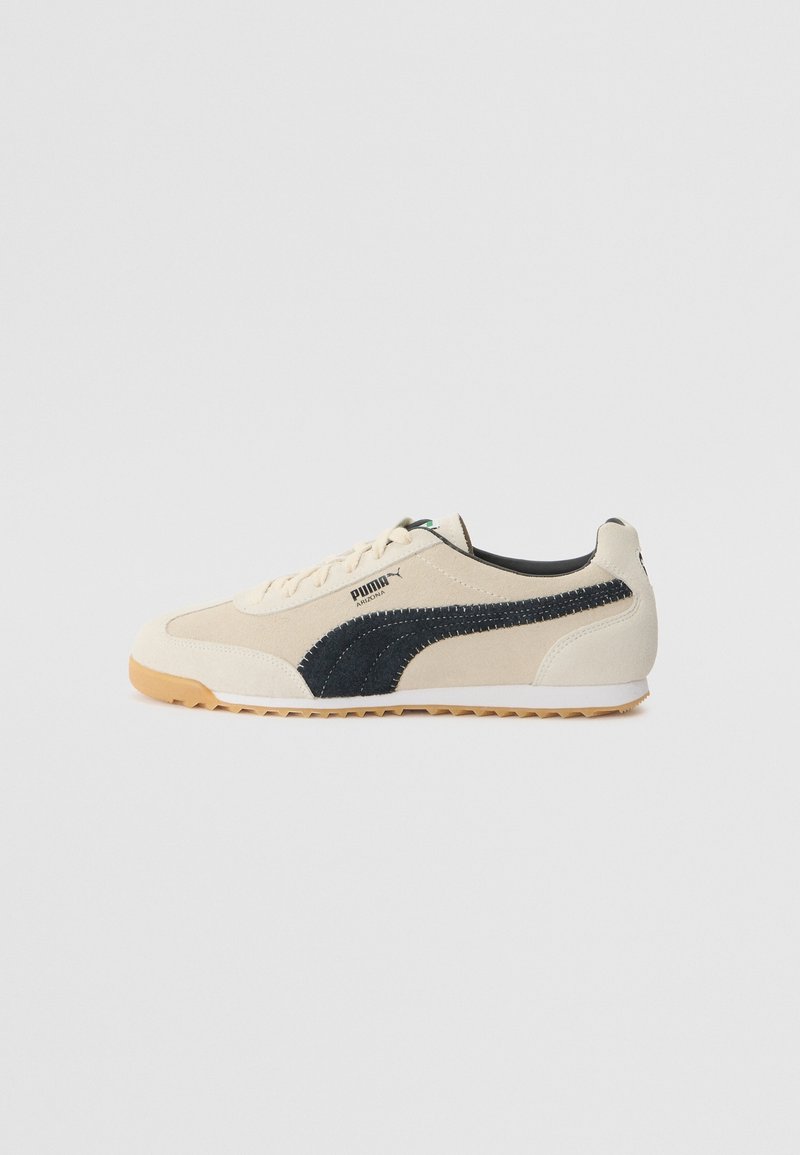 Baskets Puma Arizona beige avec bande latérale noire, semelle en gomme et design à lacets, vues de côté extérieur sur fond blanc.