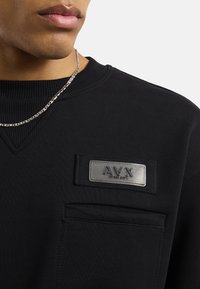 Czarny sweter z prążkowanym dekoltem, z teksturowaną metką z napisem "AV.X" oraz kieszenią z przodu, gładki materiał i czysty design.