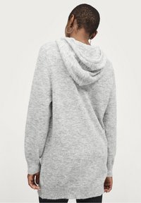 Sweat à capuche gris avec une texture douce, des manches longues et une coupe décontractée, présentant un ourlet côtelé et des détails au dos.