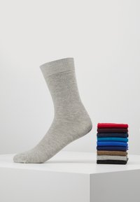 Grijze sok gemaakt van zacht materiaal met een geribde boord; daarnaast een stapel van acht verschillende sokken in rood, blauw en neutrale kleuren.