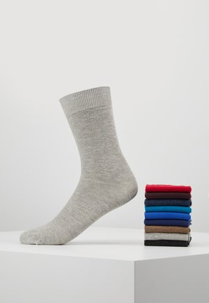 Grau gestrickte Socke aus weichem Material mit einem gerippten Bündchen; daneben ein Stapel aus acht verschiedenen Socken in Rot, Blau und neutralen Farben.