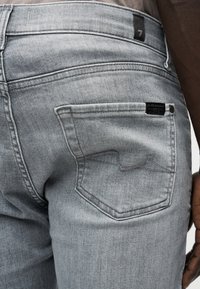 Γκρι τζιν παντελόνι από denim με ξεθωριασμένο φινίρισμα, που διαθέτει πίσω τσέπη με διακριτικό μοτίβο ραφής και ορατή ετικέτα της μάρκας στη μέση.