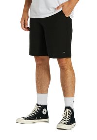 Pantaloni corti neri con taglio dritto, realizzati in un materiale morbido, dotati di tasche laterali e dettaglio del logo sulla gamba. Abbinati a sneakers nere alte.