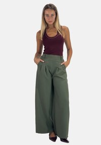 Wijde-pijp, high-waisted broeken van olijfgroene stof met zijzakken en plooien, gecombineerd met een aansluitend bordeauxrood hemd.