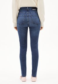 Jeans de mezclilla azul de cintura alta con un diseño ajustado, que cuentan con dos bolsillos traseros y una etiqueta de cinturón negra. Textura suave y forma entallada.