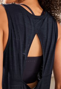 Canotta sportiva blu navy con tessuto strutturato e design posteriore a occhiello che lascia intravedere un reggiseno sportivo scuro sotto.