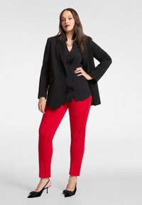 Czarny, oversize'owy blezer na czarnej koszuli zapinanej na guziki, zestawiony z dopasowanymi czerwonymi spodniami i czarnymi czółenkami na obcasie z wycięciem z tyłu, ozdobionymi kokardkami.