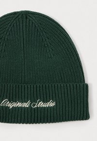 Dark green knitted beanie with ribbed texture and a folded cuff. Features white embroidered text "Originals Studio" on the cuff.