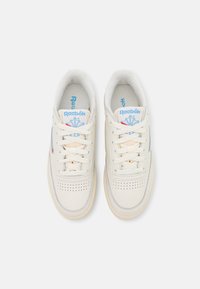 Witte leren sneakers met geperforeerde neus, platte veters, gewatteerde kraag en blauwe Reebok branding op de tong en zijkant. Crème rubberen zool.