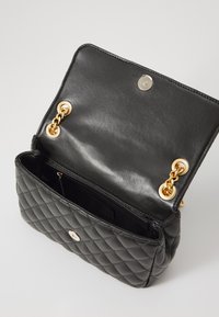 Black quilted leather handbag with gold circular hardware, a magnetic snap closure, and interior pocket. Smooth inside with chain details.