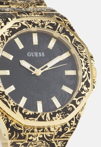 Gold-toned watch with a patterned black band, featuring a dark textured dial, gold hour markers, and a classic octagonal case design.