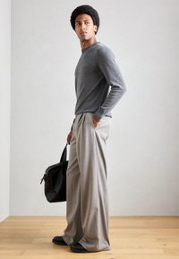 Grå ulltröja med långa ärmar, ihopparad med ljusgrå vida byxor. En svart läderväska och svarta slip-on skor fulländar looken.