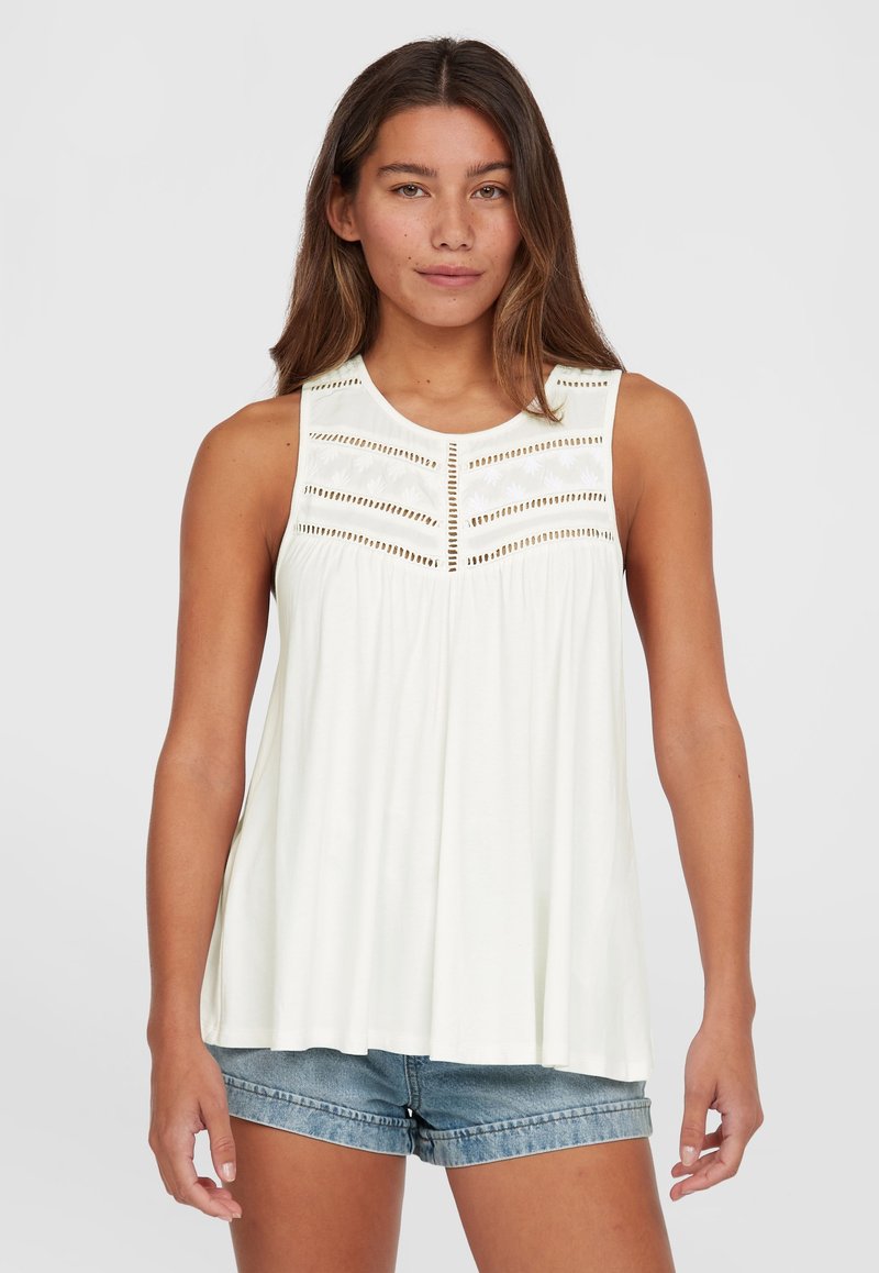 Top bianco senza maniche con colletto rotondo, caratterizzato da ritagli decorativi e dettagli ricamati sul petto, abbinato a pantaloni corti di denim.