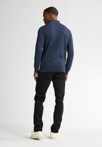 Polo shirt navy in maglia con un motivo testurizzato, abbinato a jeans neri e sneakers bianche. Sono visibili il colletto e i polsini a costine.