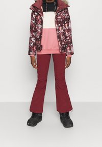 Vinterjakke med et pink og bordeaux blomstermønster, parret med en farveblokeret pink og sort sweater samt bordeaux bukser. Sorte støvler.