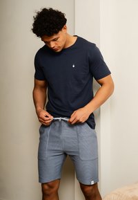 Marineblauwe t-shirt met korte mouwen en een kleine geborduurde afbeelding, gecombineerd met lichtblauwe textuur shorts met een drawstring taille en twee voorzakken.