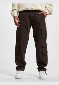Pantalones cargo marrones con múltiples bolsillos laterales, puños elásticos y un corte relajado, combinados con zapatillas blancas.