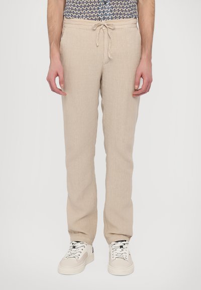 Beige linnedragt med en afslappet pasform, der har elastisk talje og snøre, kombineret med hvide sneakers og en mønstret skjorte.