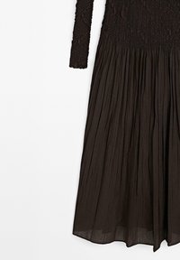 Black long-sleeve dress featuring a smocked top and a pleated skirt. Made of lightweight material with a textured surface.