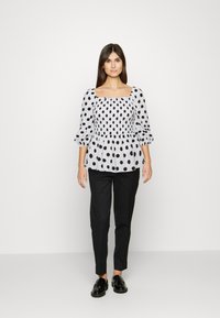 Top preto e branco com bolas de poá, decote quadrado e mangas bufantes, combinado com calças pretas ajustadas e mocassins pretos.