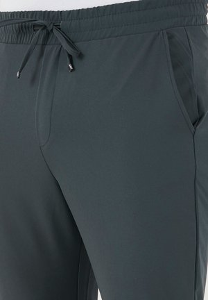 Pantalons de sport gris foncé avec une taille élastique, fermeture par cordon de serrage et poches latérales. Texture lisse et coupe ajustée pour le confort.