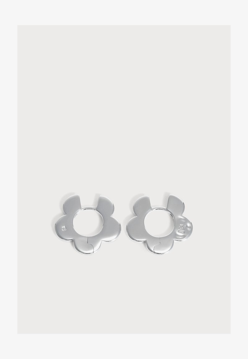Paire de boucles d'oreilles créoles en forme de fleur de couleur argentée avec cinq pétales arrondis sur un fond gris clair.