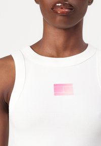 Weißes, geripptes Tanktop mit einem Farbverlauf-Design in Pink auf der Brust. Glatte Textur, figurbetonter Schnitt, runder Halsausschnitt, ärmellos.