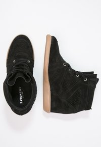 Paire de baskets compensées en daim noir avec semelles marron, l'une vue de dessus et l'autre de côté, sur fond blanc.