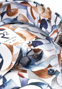 Gemustertes Hemd mit weißem Hintergrund und abstrakten Formen in Blau, Braun und Grau. Enthält Knöpfe und ein Etikett am Kragen.