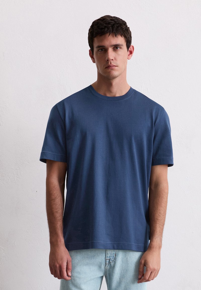Marineblauwe katoenen T-shirt met ronde hals en korte mouwen, rechte pasvorm, gladde textuur, gecombineerd met lichtblauwe jeans.