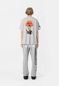 Camiseta gris con un gráfico de un perro de dibujos animados en un traje de artes marciales. Combinada con pantalones de chándal grises que muestran un logotipo. Diseño casual.