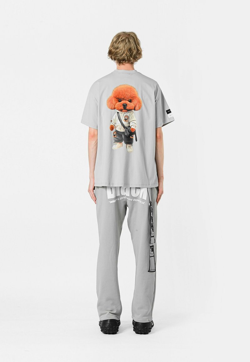 Camiseta gris con un gráfico de un perro de dibujos animados en un traje de artes marciales. Combinada con pantalones de chándal grises que muestran un logotipo. Diseño casual.