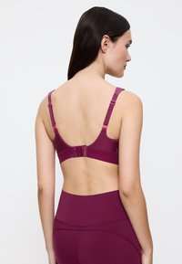 Tummanpunainen rintaliivit säädettävillä olkaimilla, hakaset ja silmukat suljennassa sekä hillityt leikkauskoristeet. Sileä kangas ja saumaton muotoilu.