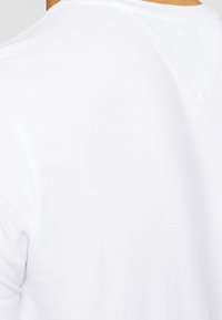 White cotton T-shirt with a V-neck design, featuring soft fabric texture and minimalistic style. No visible patterns or embellishments.