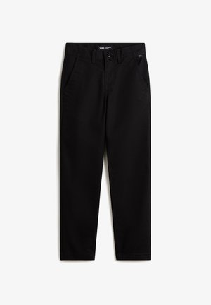 Personne portant un t-shirt Vans blanc, un pantalon noir, des baskets Vans bleues, avec un sweat à capuche violet à carreaux noué autour de la taille.