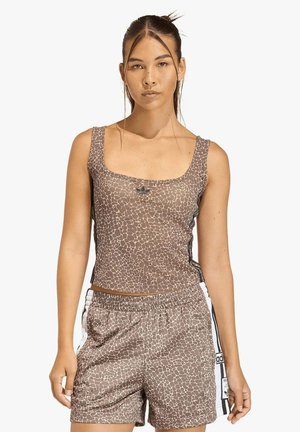 Femme aux longs cheveux foncés portant un crop top marron à motif et un short de sport assorti avec des bandes blanches sur les côtés et le logo Adidas.
