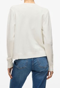 Maglione bianco lavorato a maglia con orlo e polsini a coste, caratterizzato da una vestibilità rilassata. Indossato con jeans in denim blu.