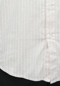 Biela košeľa na zapínanie s tenkými vertikálnymi sivými pruhmi, zastrčená do čiernych nohavíc.