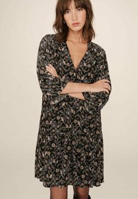 Robe noire à fleurs avec un décolleté en V profond, des manches 3/4 et une jupe évasée. Présente des motifs de fleurs pastel avec des accents bleus et beiges.