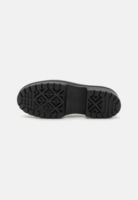 Black shoe sole with a textured rubber bottom featuring a geometric pattern for traction. The design includes a flat profile and sturdy construction.