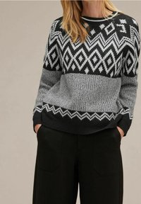 Stickad tröja i svart och grått med geometriska mönster. Har en rundad halsringning, ribbade ärmslut och en texturerad kropp.