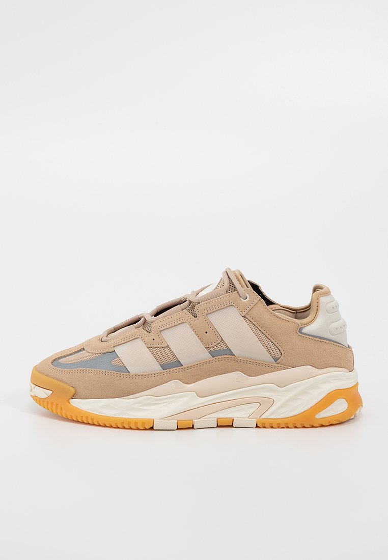 Beige Sneaker mit Obermaterial aus Mesh und Wildleder, drei tonale Streifen, Gummisohle mit orangefarbenen Akzenten und strukturierten Details an der Zwischensohle.