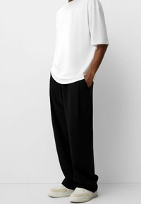 Hvid kortærmet t-shirt parret med sorte brede bukser og lyse sneakers. Glat stof, afslappet pasform og enkelt design.