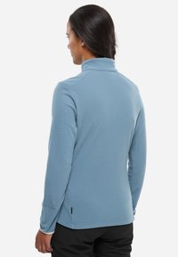 Veste en polaire bleu clair avec un col haut et des manches longues. Présente une surface texturée et des accents latéraux discrets.