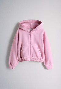 Světle růžová mikina na zip s kapucí, přední kapsou ve stylu klokánka, elastickým lemem a žebrovanými manžetami, zobrazená na jednoduchém šedém pozadí.
