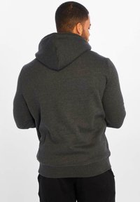 Un sweat à capuche gris foncé avec un cordon de serrage, des poignets côtelés et une coupe décontractée. Le tissu semble doux et texturé avec des détails de couture subtils.